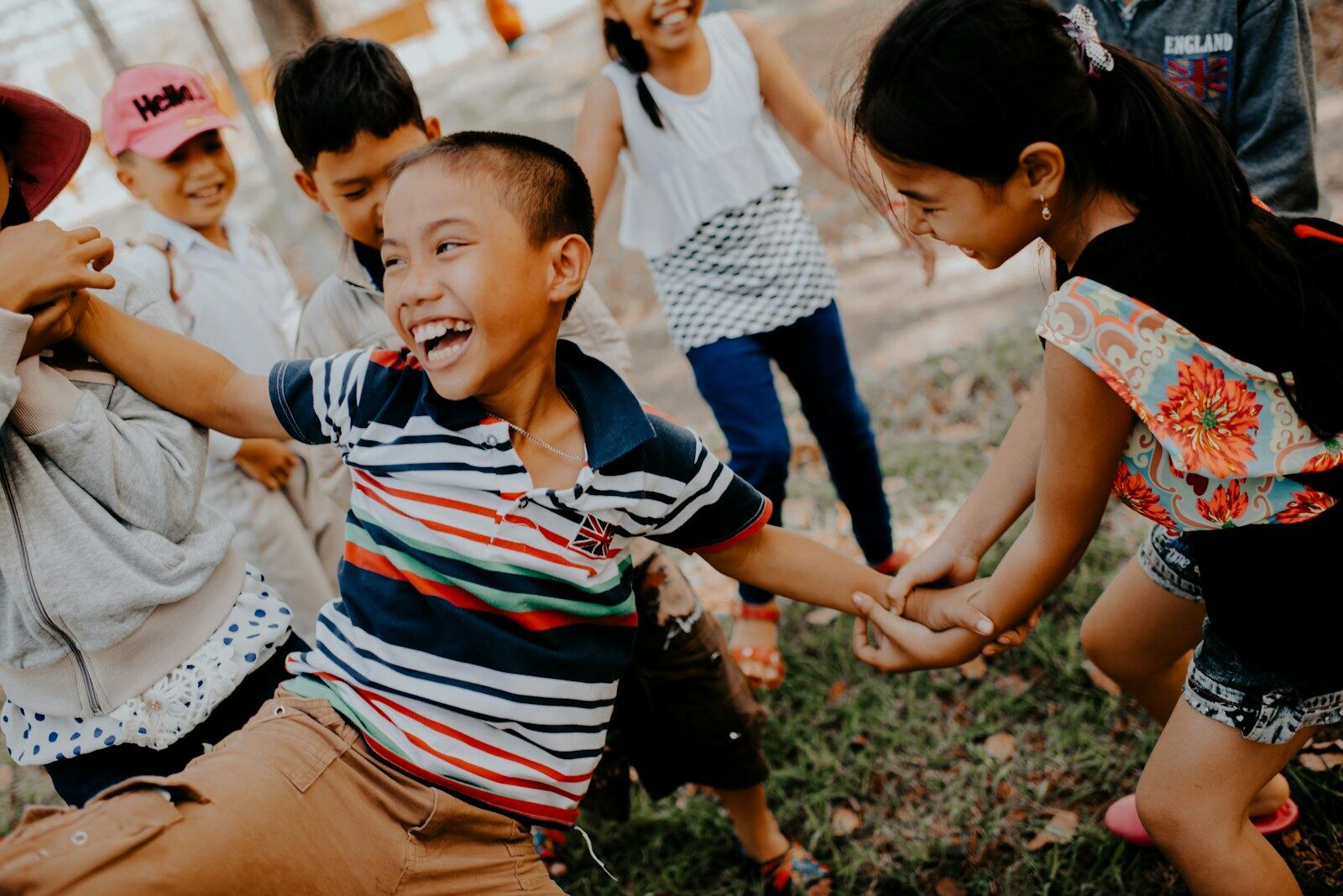 A group of children laughing as they play a circle game outdoors, holding hands.