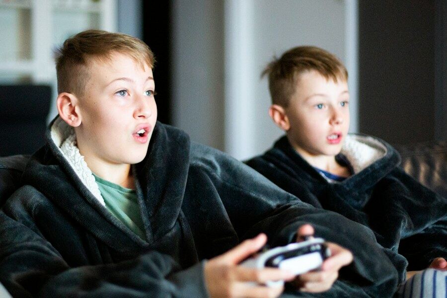 Two boys on a couch, wide-eyed and absorbed in a video game.